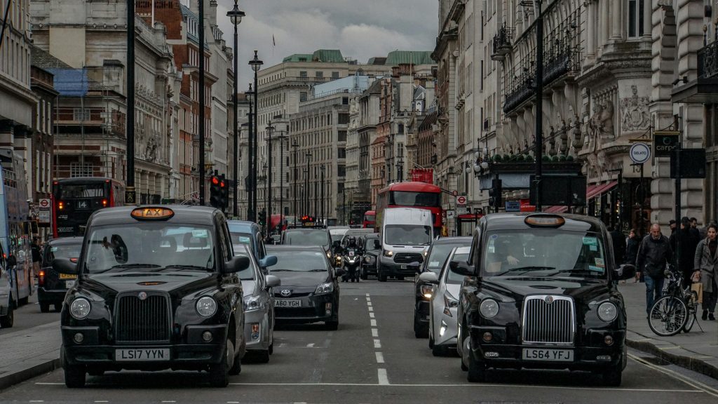 Busy city street with classic black taxis, cars, and pedestrians in an urban area
